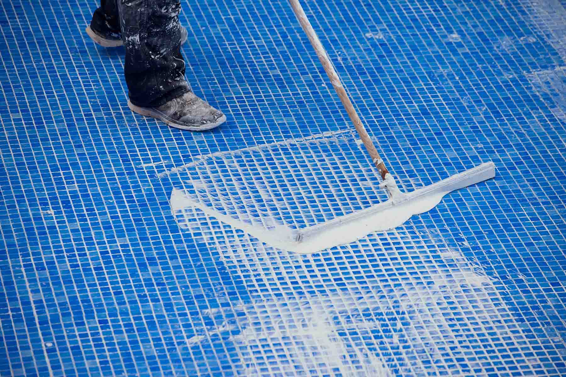 Worker covering seames on the tile in the pool. Pool repairing work