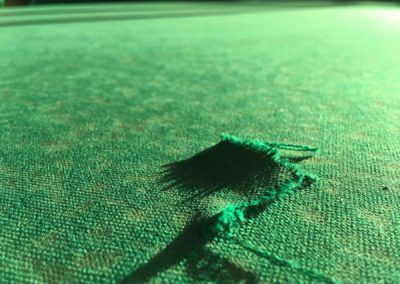 Damage to the pool table. Torn cloth on the pool table
