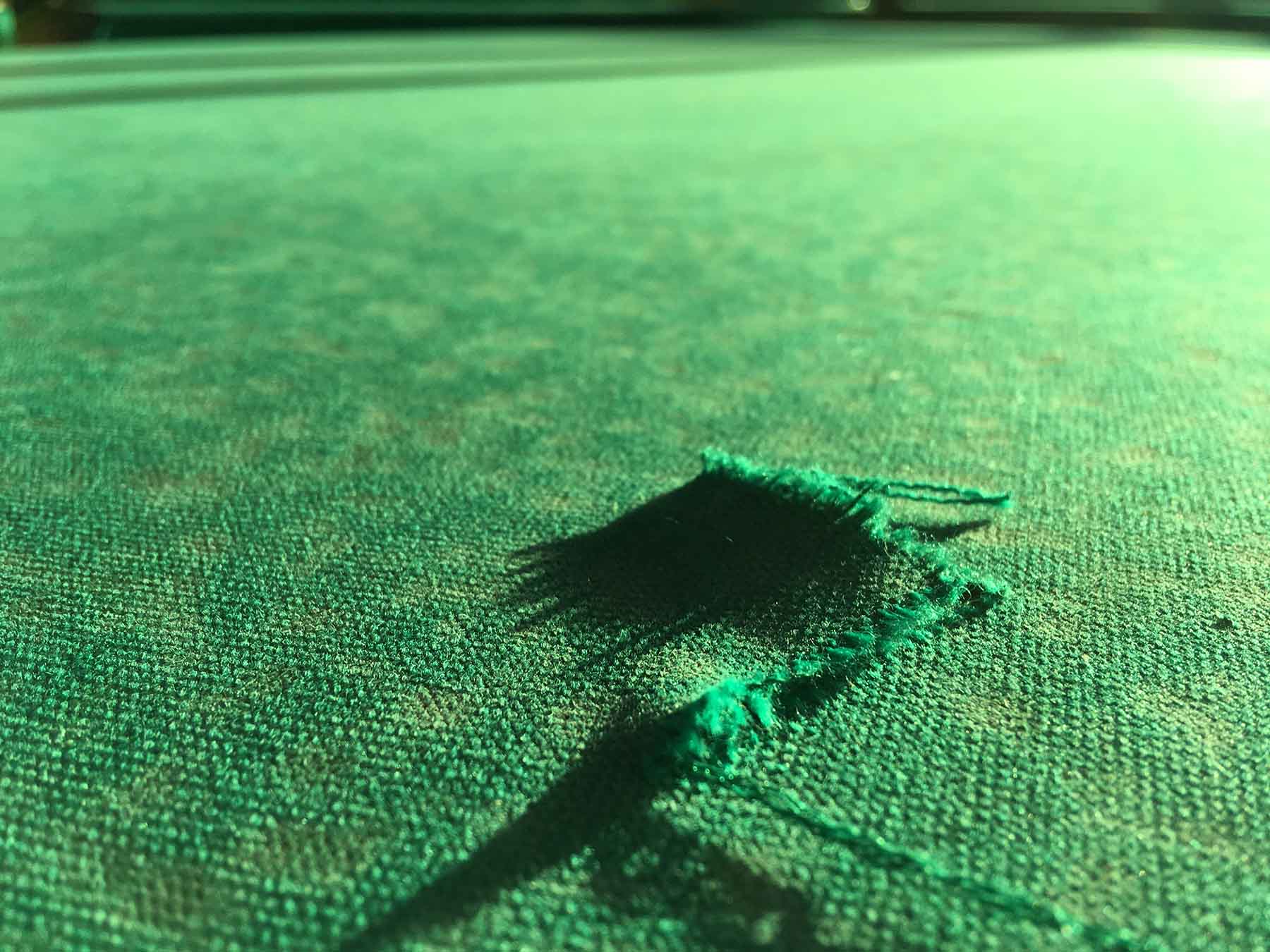 Damage to the pool table. Torn cloth on the pool table